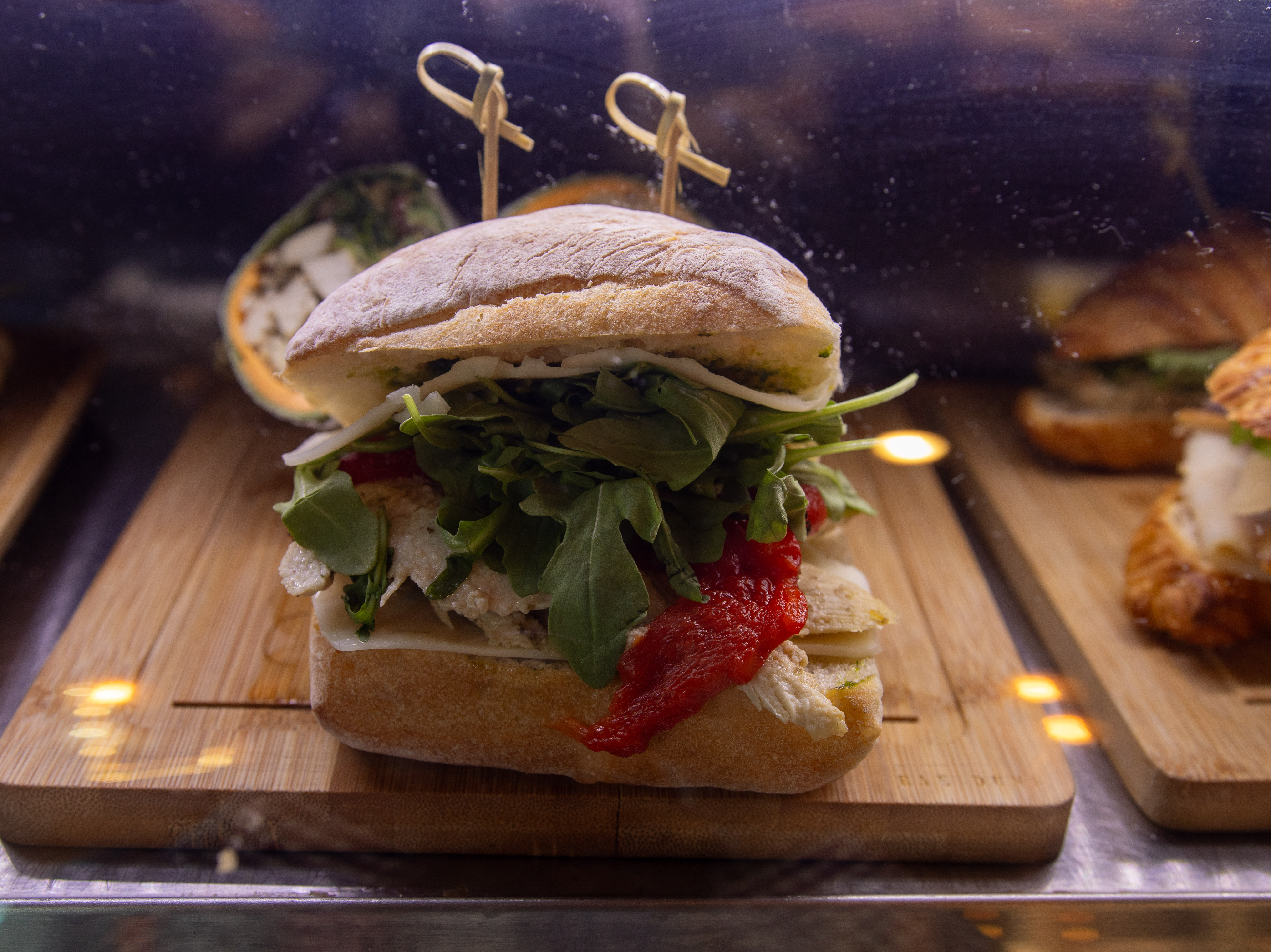 A close-up of a sandwich filled with greens, red peppers, and mozzarella, served on a wooden board.