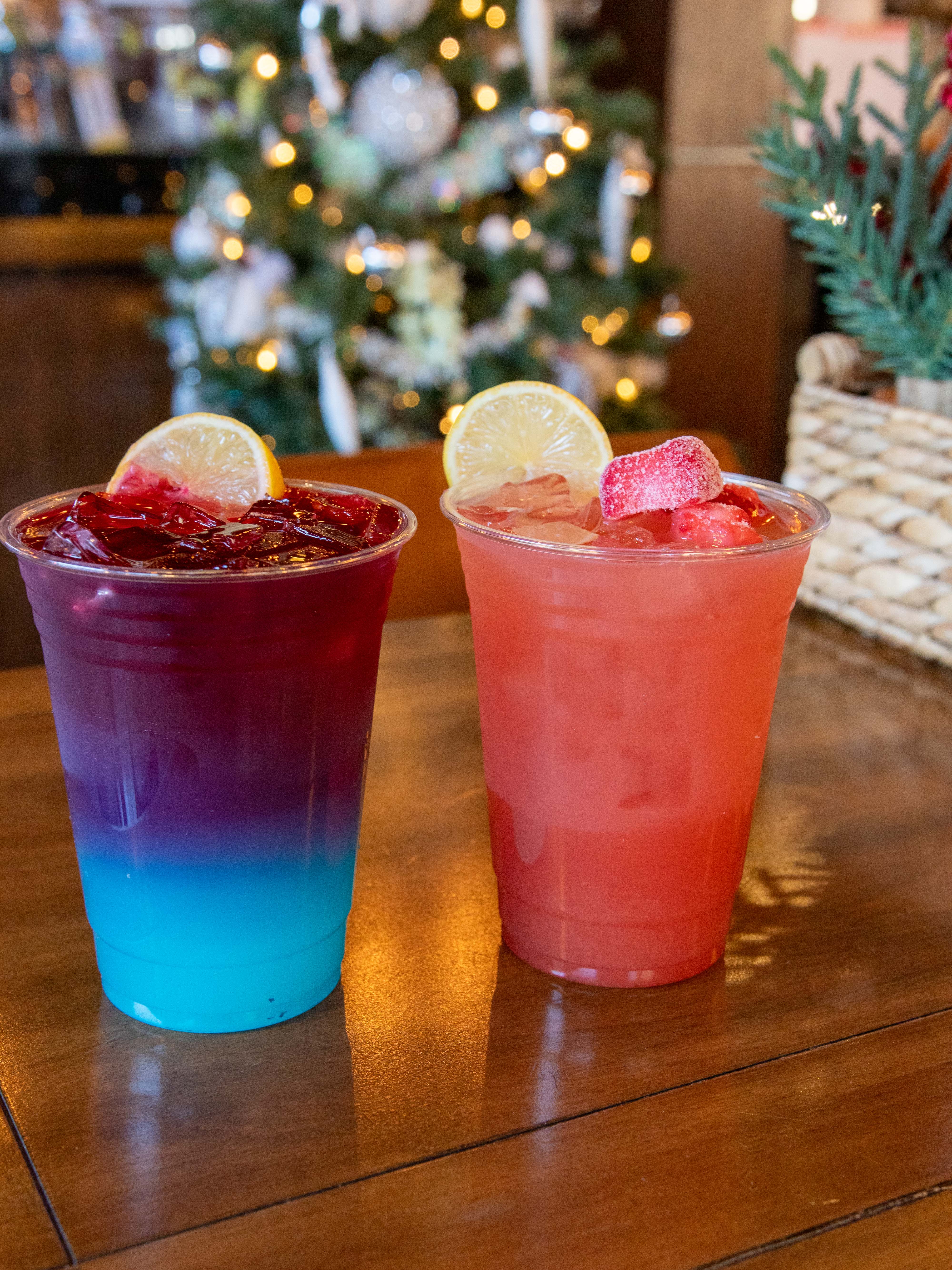 Two colorful drinks in cups on a table with a Christmas tree in the background.
